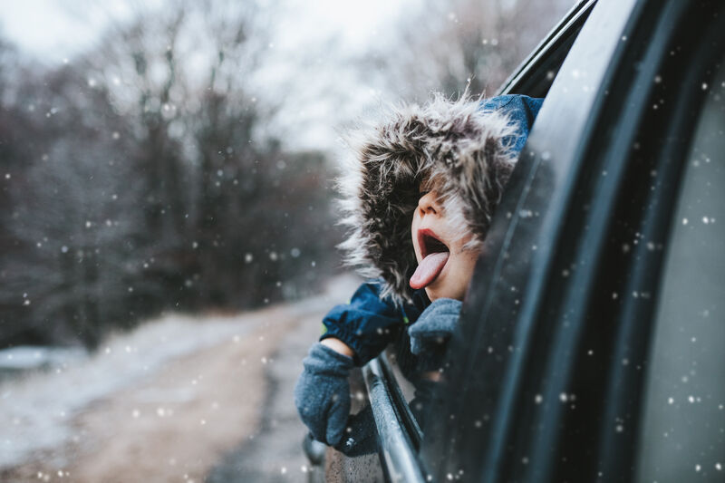 Child sticking head out of car window trying to catch snow on their tongue