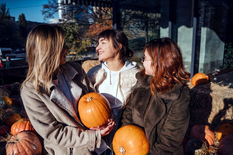 Women holding pumpkins laughing together outdoors