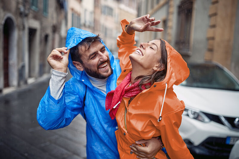 Couple playing in the rain with a white car in the background of them both