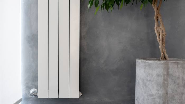 A vertical white electric radiator on the wall next to a plant