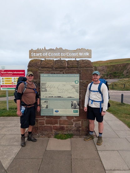 Two men standing in front of a sign marking the start of the Coast-to-Coast walk from Cumbria and North Yorkshire
