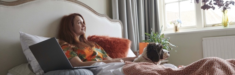 Woman sitting on bed with laptop and dog