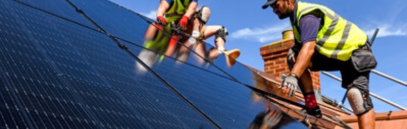 Two installers installing black solar panels onto a roof 