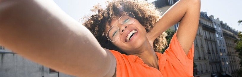 Happy person outside in orange tee with arm outstretched 