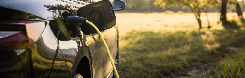 EV getting charged on a sunny day with a field in the background