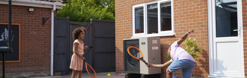 Brother and sister playing tennis in the garden nearby an air source heat pump