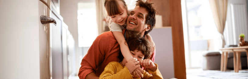 Dad playing with his kids on the floor with sunlight coming in through the windows and doors