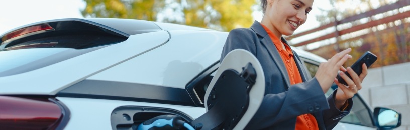 Woman charging her EV while smiling at her phone