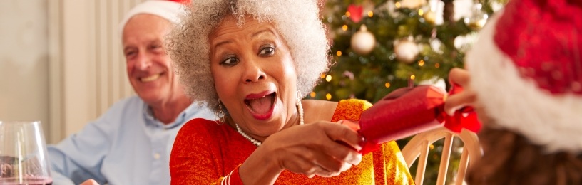 Happy lady pulling Christmas cracker at dinner table, tree in background