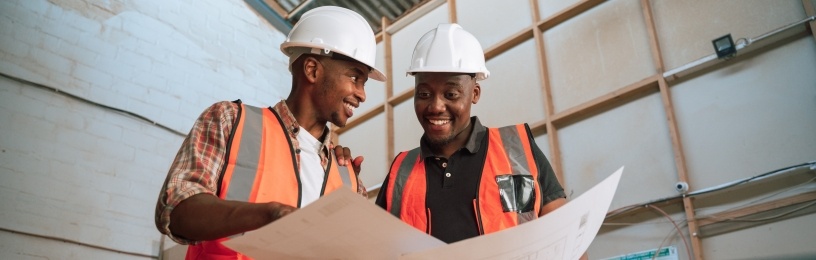 Two people looking at plans in hard hats and high vis