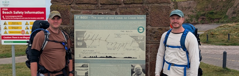 Two men standing in front of a sign marking the start of the Coast-to-Coast walk from Cumbria and North Yorkshire