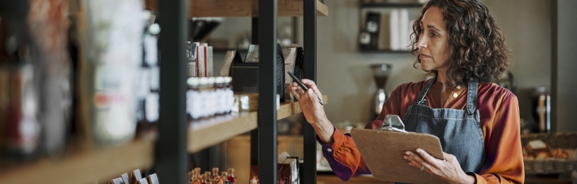 A shop owner doing a stock check of shelves in a deli