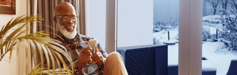 Man sitting inside cosy home with ashp unit outside
