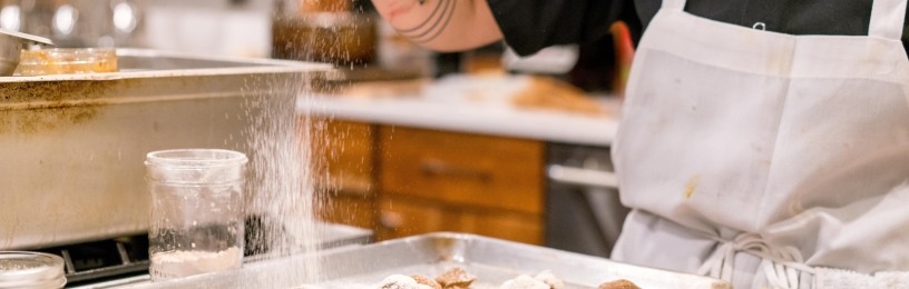 A man sifting icing sugar over cakes