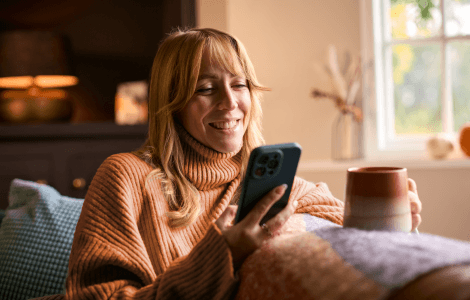 Woman looks at phone with mug in hand