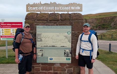 Two men standing in front of a sign marking the start of the Coast-to-Coast walk from Cumbria and North Yorkshire