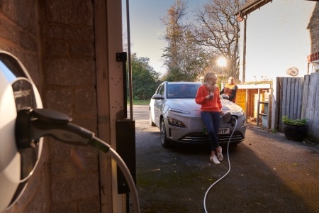Woman sitting on bonnet of EV whilst it's charging.