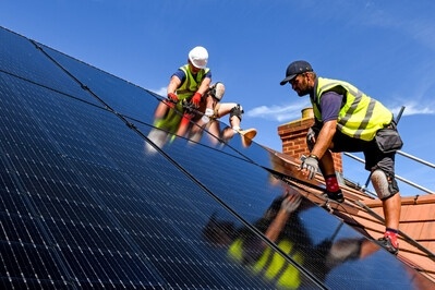 Two installers installing black solar panels onto a roof 