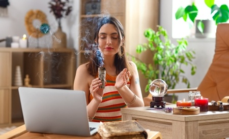 Woman with a laptop and crystal ball smoking sage