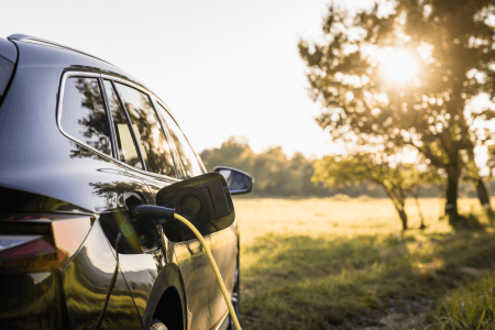 EV getting charged on a sunny day with a field in the background
