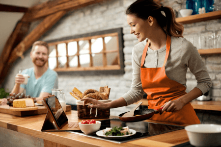 Couple in kitchen with woman cooking looking at a tablet