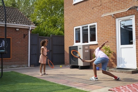 Brother and sister playing tennis in the garden nearby an air source heat pump