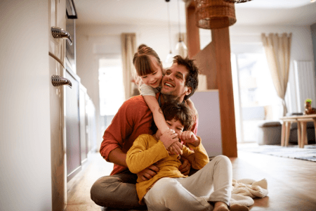 Dad playing with his kids on the floor with sunlight coming in through the windows and doors