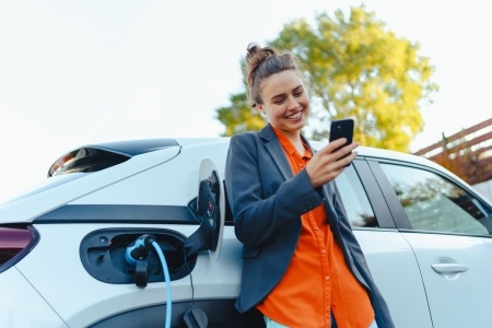 Woman leaning against EV plugged into a charger