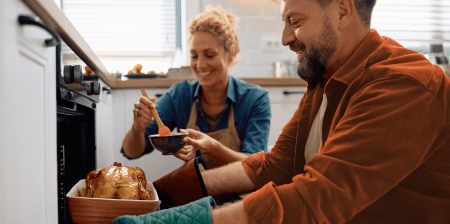 Husband taking roast out of the oven while wife looks on