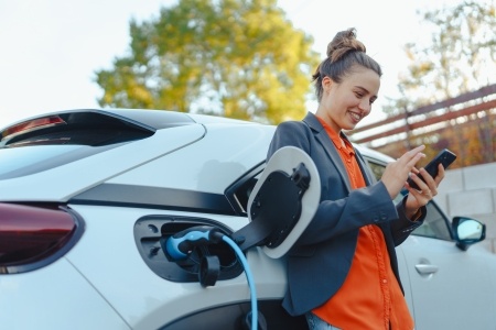 Woman charging her EV while smiling at her phone