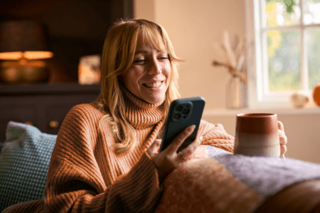Woman looks at phone with mug in hand