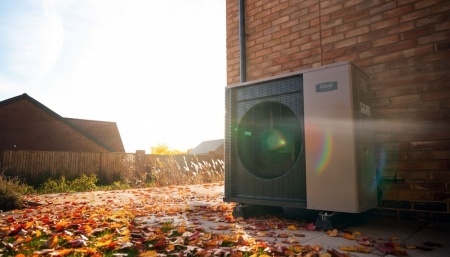 Heat pump on the outside of a house with autumn leaves on the ground