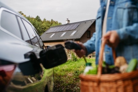 person plugging in EV with house and solar panels visible  