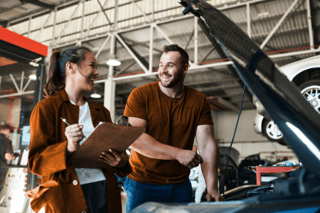 2 people in a garage next to a car with an open bonnet