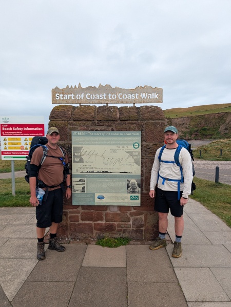 Two men standing in front of a sign marking the start of the Coast-to-Coast walk from Cumbria and North Yorkshire