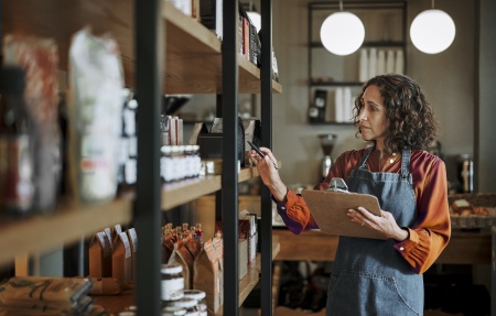 A shop owner doing a stock check of shelves in a deli