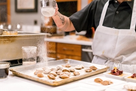 A man sifting icing sugar over cakes