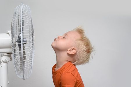 Boy cooling his face with an electric fan