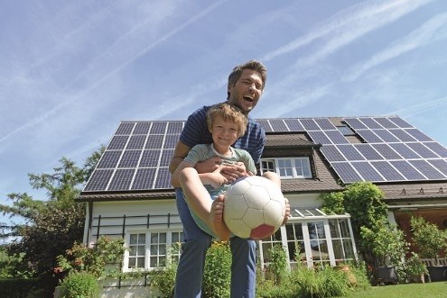 Solar panels on roof of detached family home with father and son playing football in front