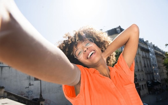 Happy person outside in orange tee with arm outstretched 