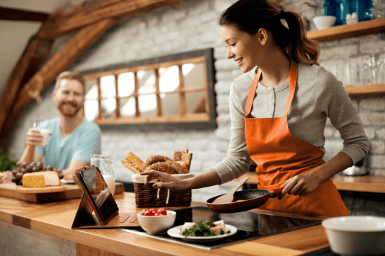 Couple in kitchen with woman cooking looking at a tablet