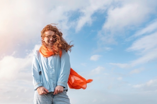 Woman with an orange scarf blowing in the wind, in front of a big blue sky