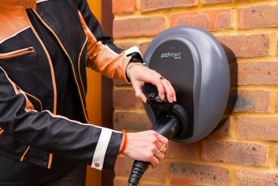 Person in black and orange coat using a tethered Pod Point EV home charger