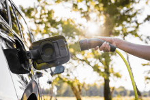 Plugging in a charger into an electric vehicle with a sunny backdrop of trees