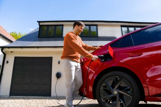 Man in an orange jumper charging his red EV outside of his home