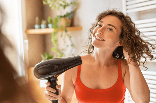 Woman using a hair drier to dry her hair in an orange vest top