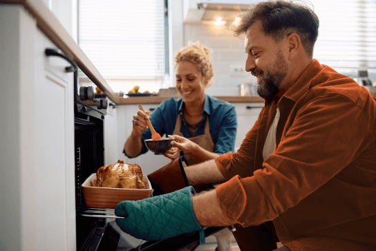 Husband taking roast out of the oven while wife looks on