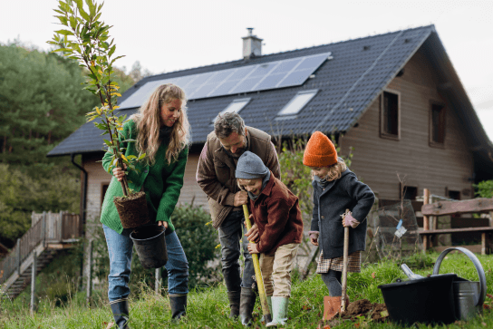 A family of two parents and two children gardening in front of their home with solar panels on the roof. The which? trusted trader logo is next to them.