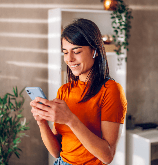 Female in orange t shirt looking at her mobile phone smiling