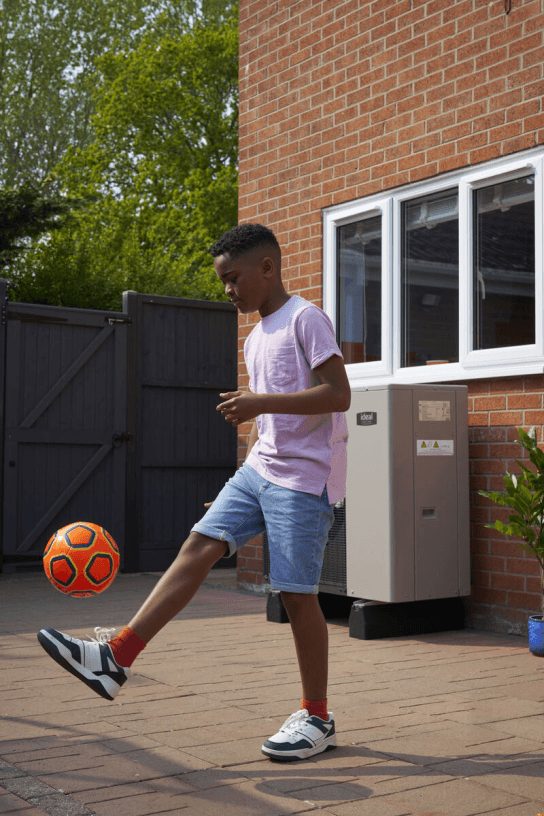 boy kicking football in front of heat pump